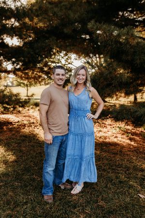 Smiling young couple posing together outdoors in front of pine trees during golden hour.