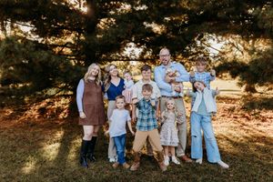 Large extended family posing together outdoors under pine trees during golden hour photography session.