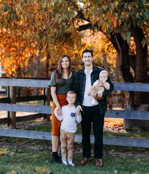 Family of four poses by wooden fence surrounded by vibrant autumn foliage.