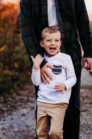 Happy young boy laughs while standing with his father on an autumn outdoor path.