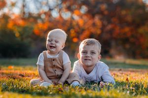 Two young brothers sit together on grass smiling in warm autumn sunlight.