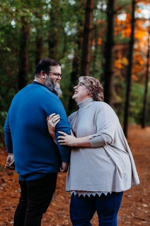 Laughing middle-aged couple embracing each other on a forest path with colorful autumn foliage.