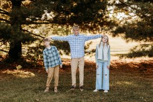 Teen boy playfully stretching arms over younger siblings during outdoor fall family photo session.