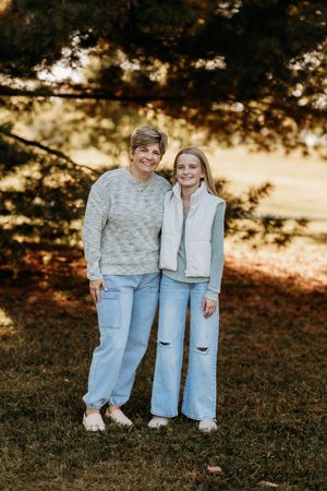 Mother and preteen daughter smiling together outdoors in matching casual blue outfits during fall.