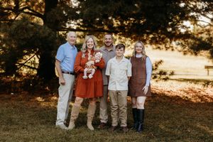 Family of five posing outdoors in autumn earth tones with pine trees in background.