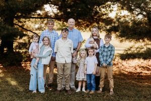 Extended family group portrait outdoors under pine trees during warm golden hour fall session.