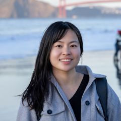 A young Asian woman smiles warmly at Baker Beach with the Golden Gate Bridge visible in the soft background.