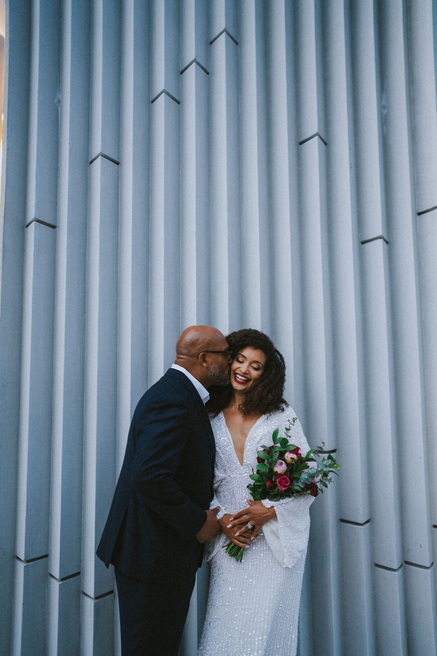Wedding ceremony in greenhouse-style venue with hanging floral arrangements and seated guests.