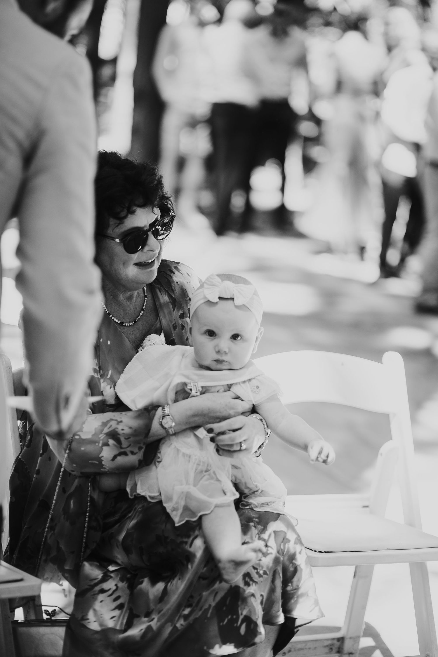 Black and white photo of a grandmother holding a baby girl in a white dress at a wedding.