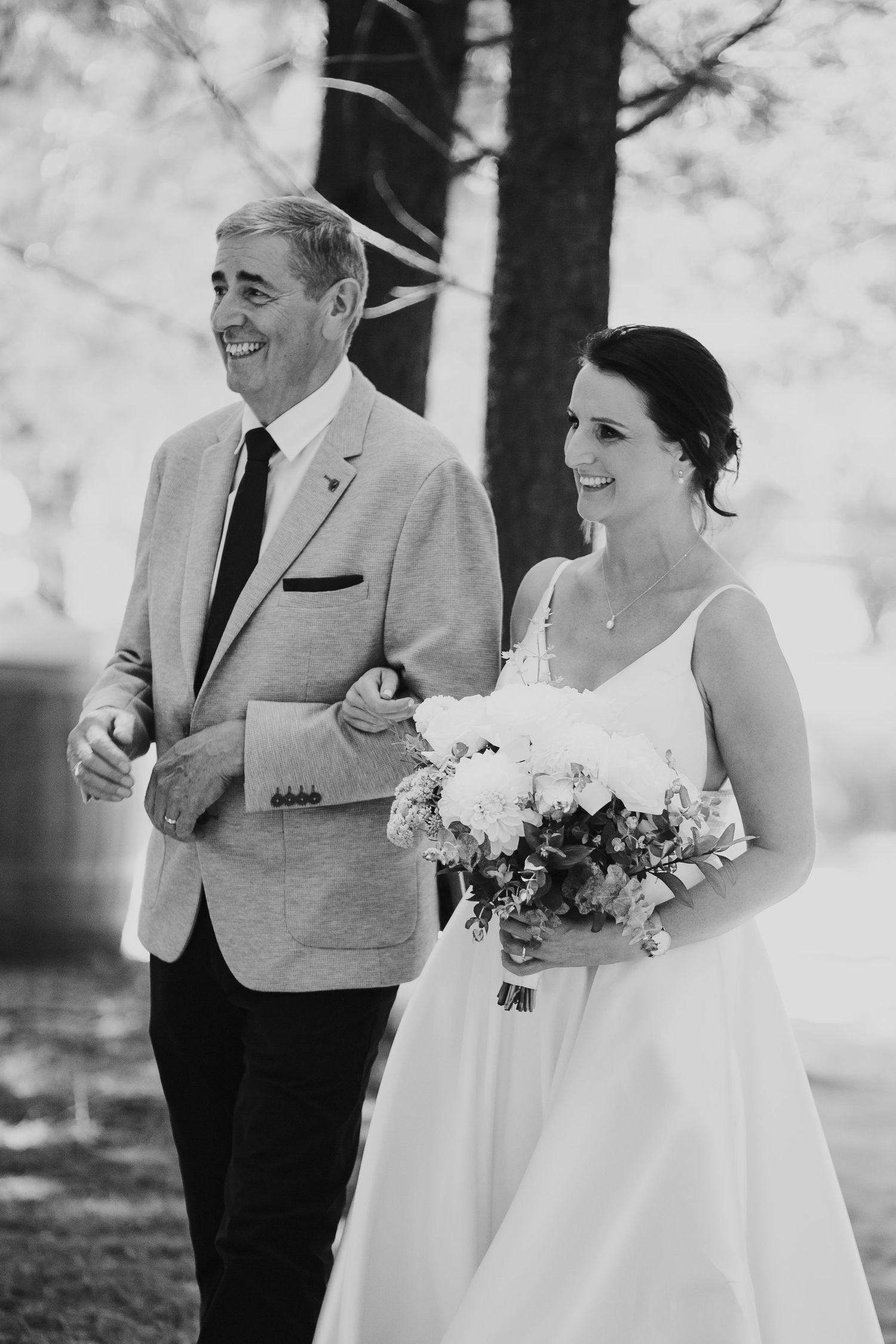 Black and white photo of a joyful bride and her father walking down the wedding aisle.