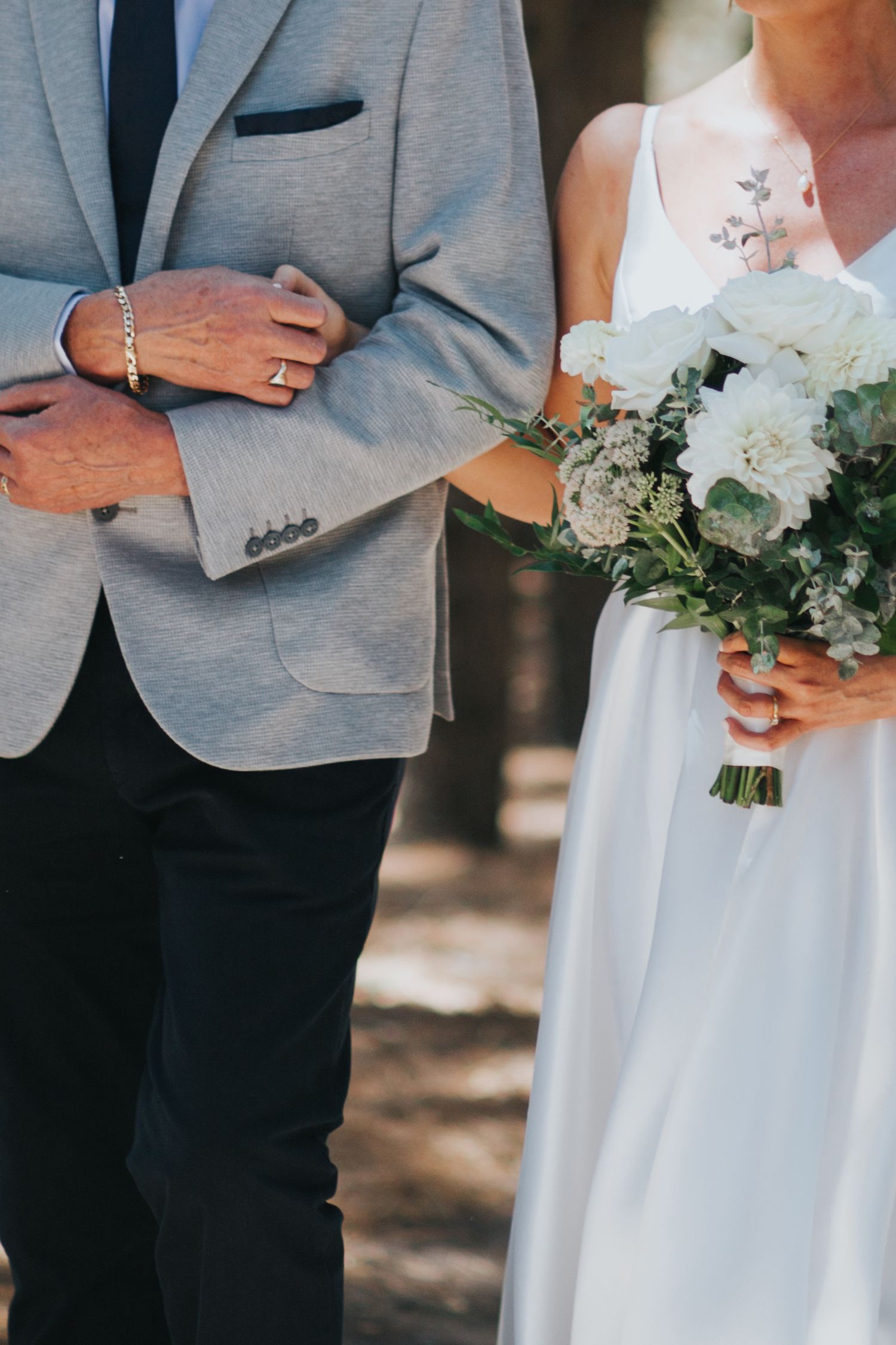 Close-up of a bride holding white floral bouquet while walking arm in arm with her father.