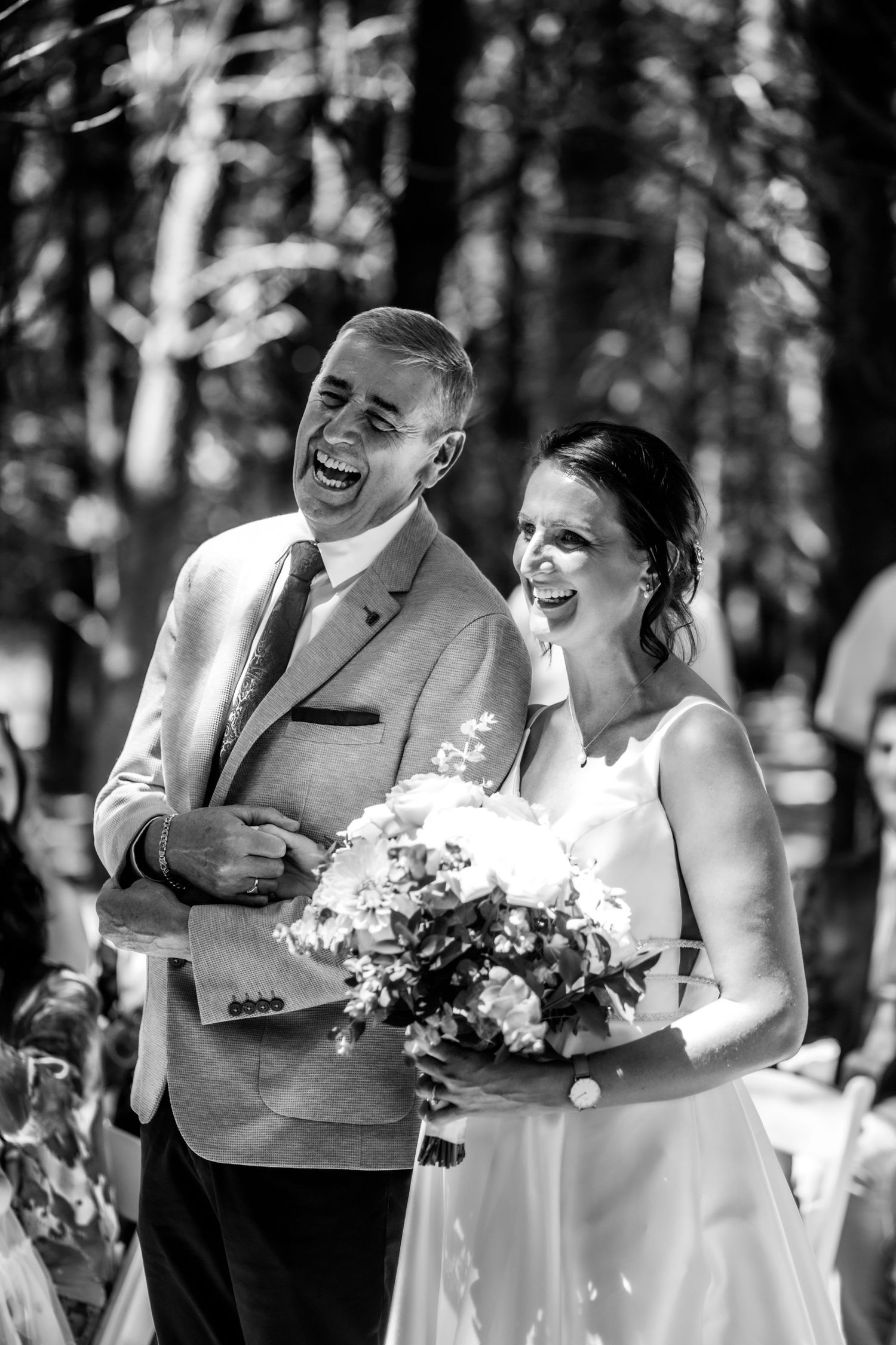 Bride and escort laugh joyfully walking down forest wedding aisle, bride holding floral bouquet.