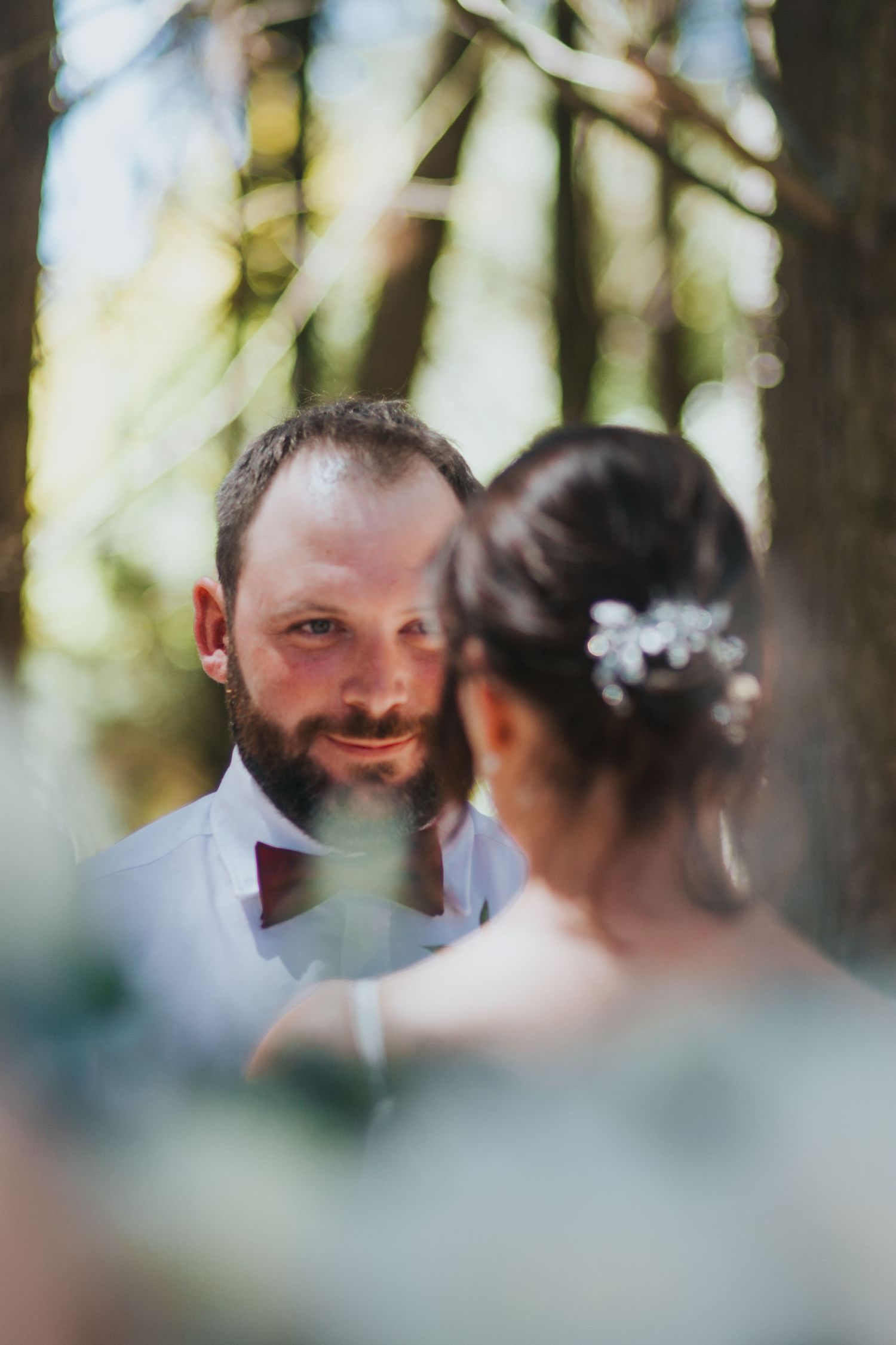 Bearded groom gazes lovingly at bride during intimate outdoor forest wedding ceremony exchange.