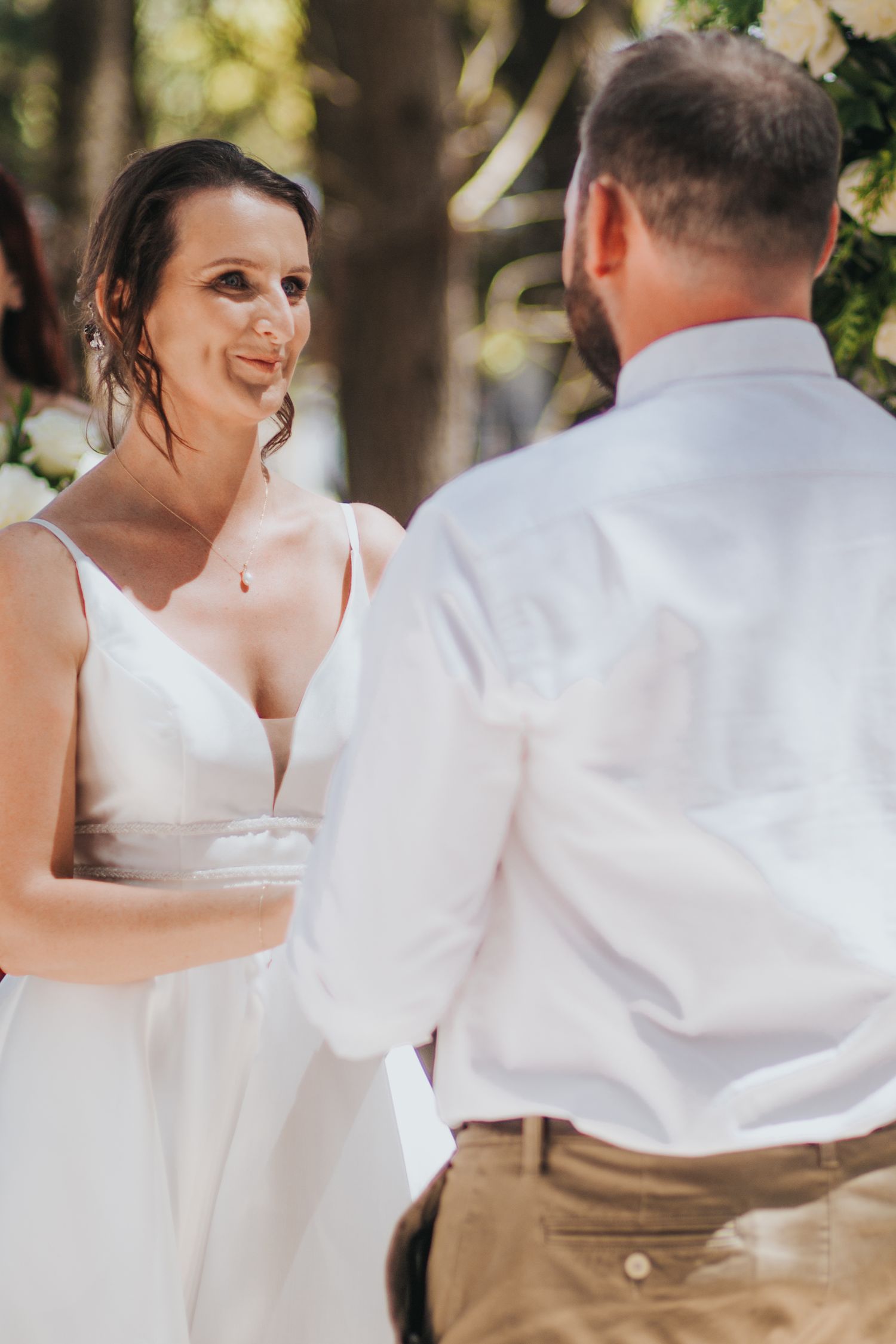 Emotional bride gazes at groom while holding hands during outdoor wedding ceremony in forest.