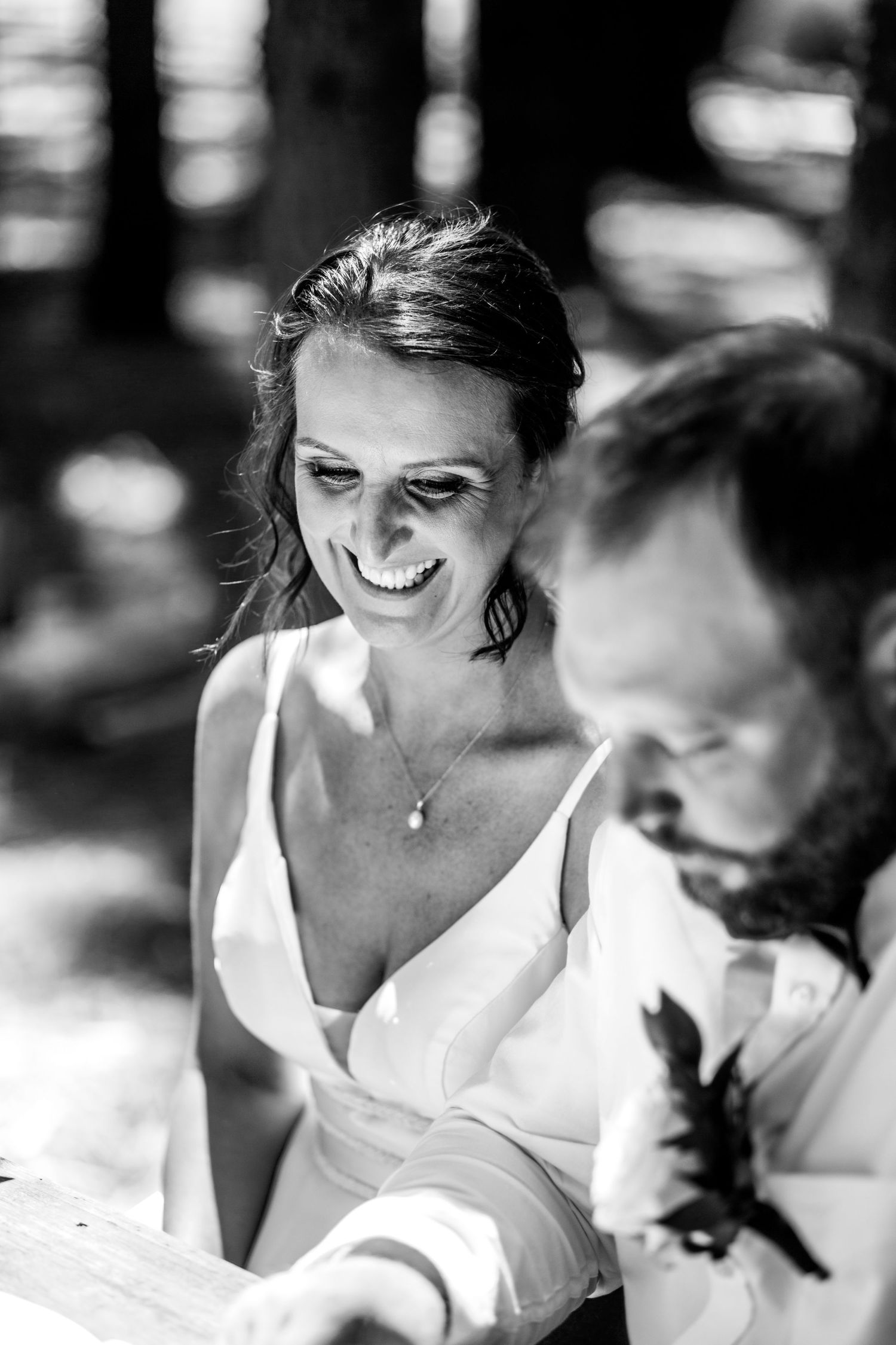 Bride smiling joyfully in a white dress during an outdoor wedding ceremony in black and white photography.