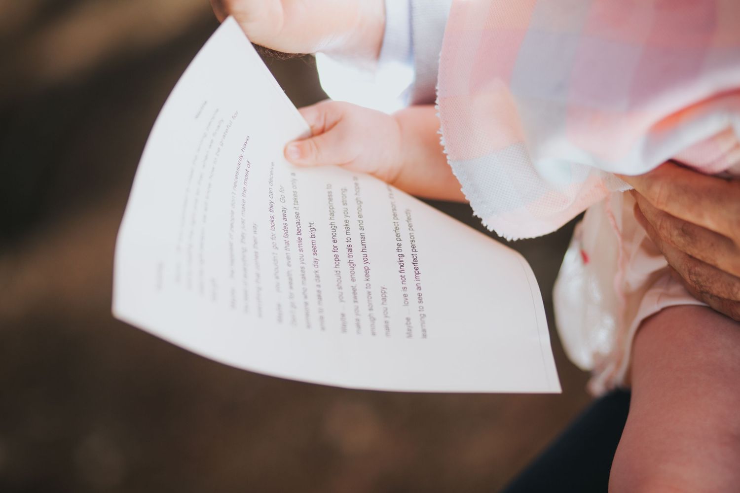 Close-up of hands holding a wedding ceremony program card with printed vows outdoors.