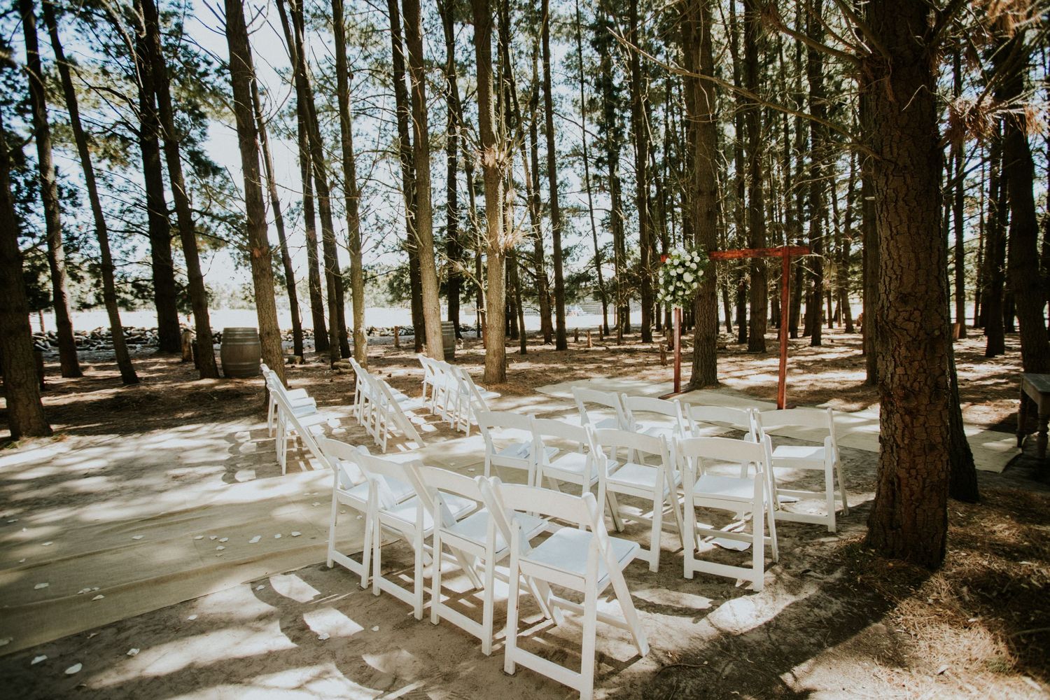 White folding chairs arranged in rows for an outdoor forest wedding ceremony on a sunny day.