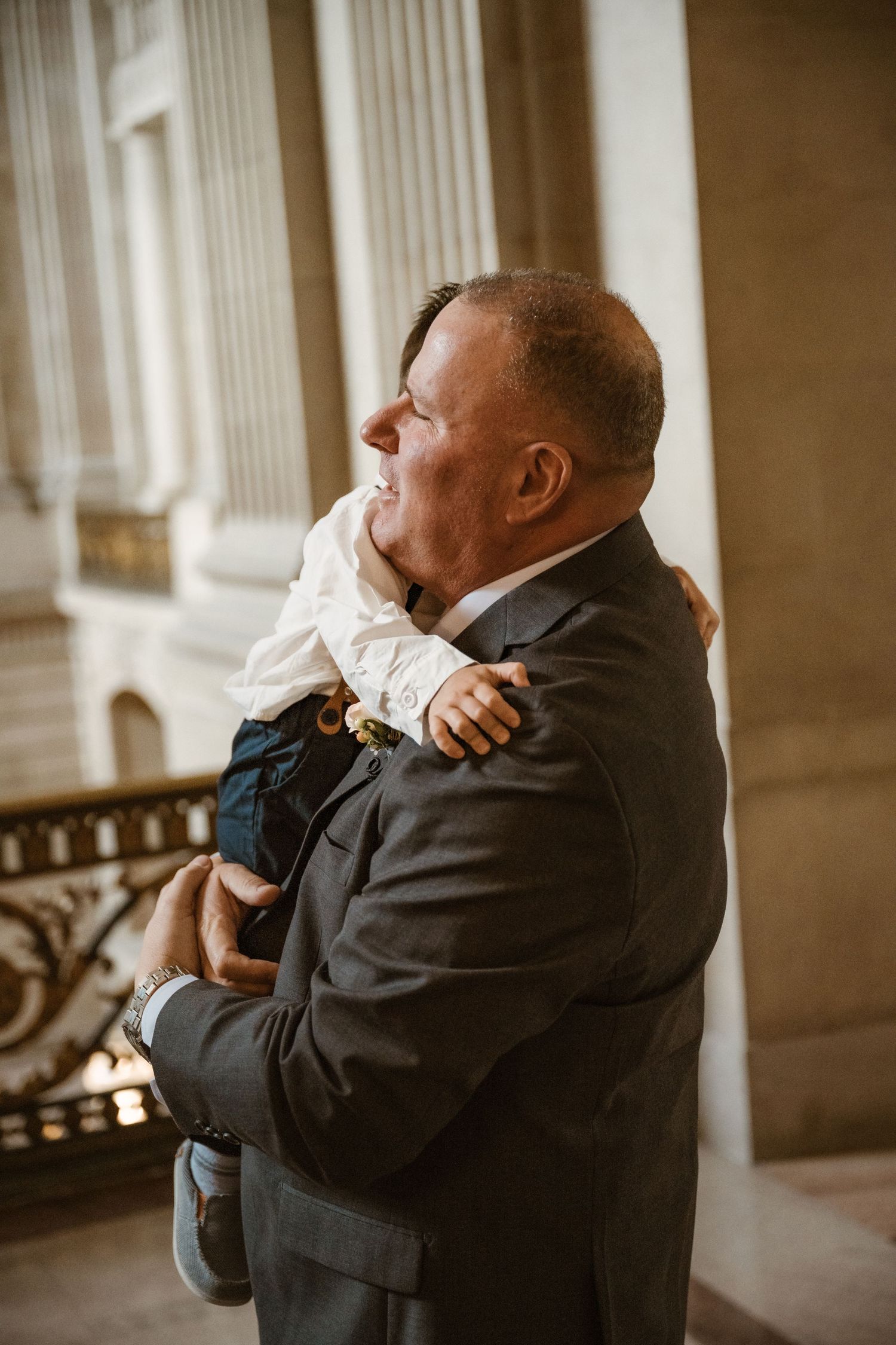 An emotional first look moment captured between two people embracing in a grand columned hallway.