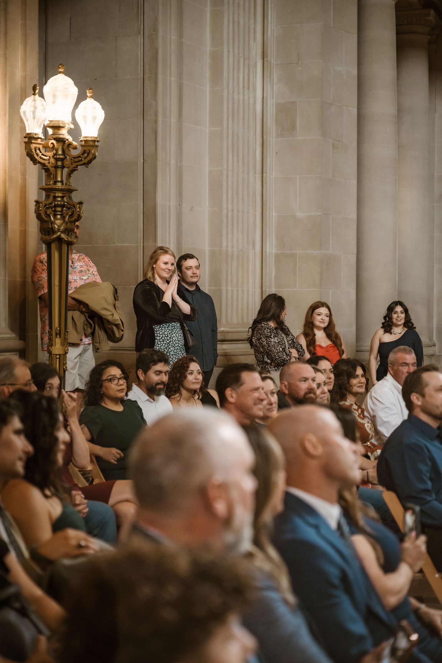 Crowd of wedding guests seated in formal attire under elegant chandeliers.