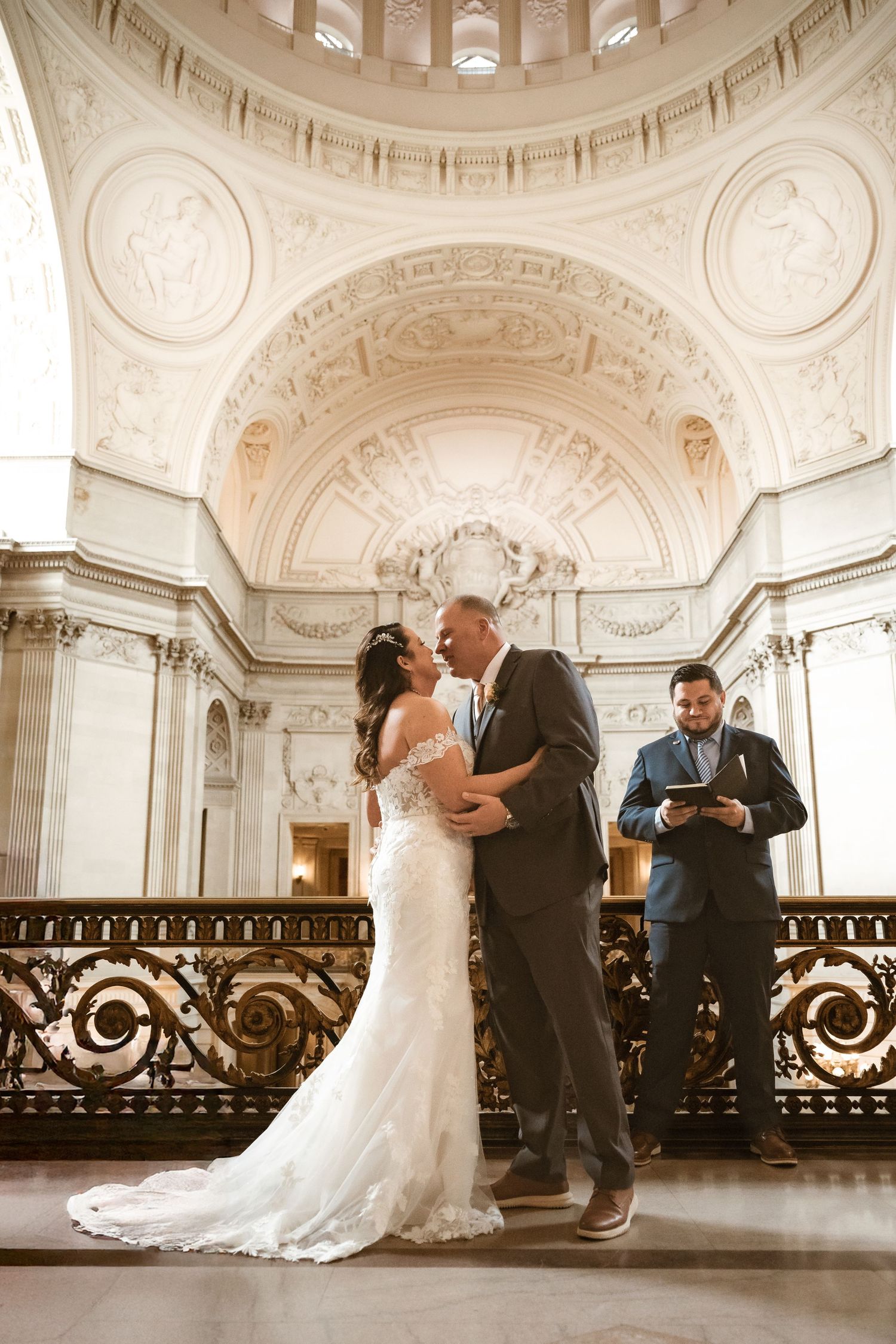 Wedding ceremony in grand historic venue with decorative ceiling and ornate railings.
