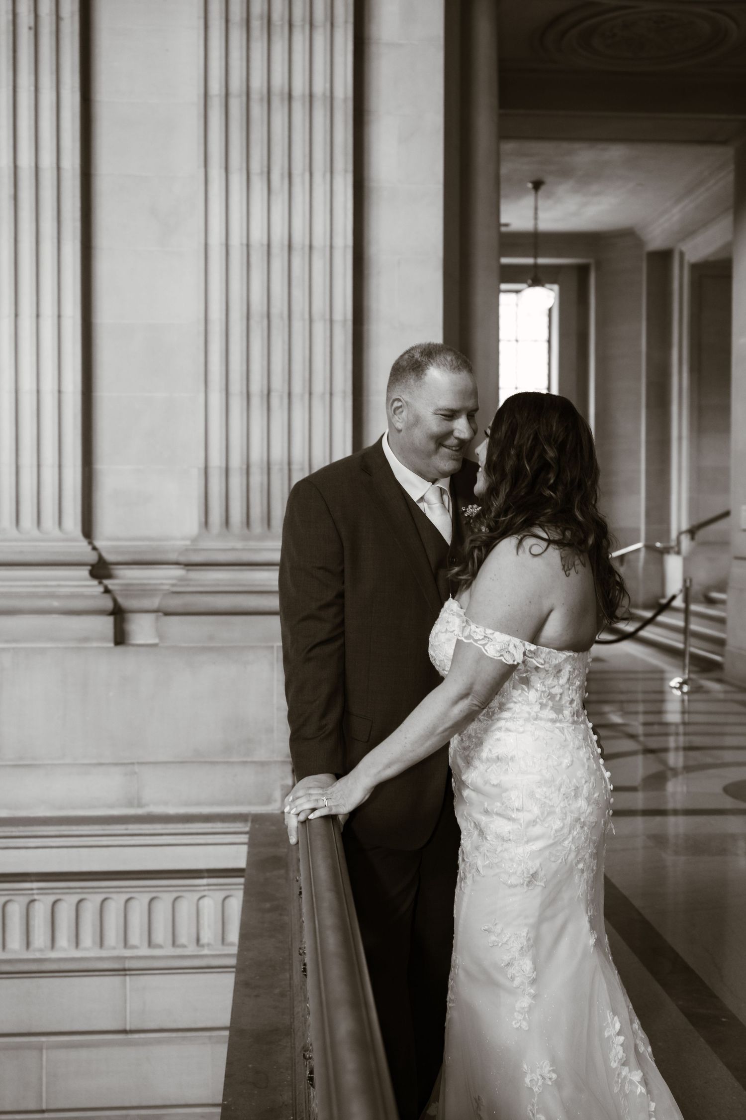 Black and white wedding photo in elegant hallway with classical columns.