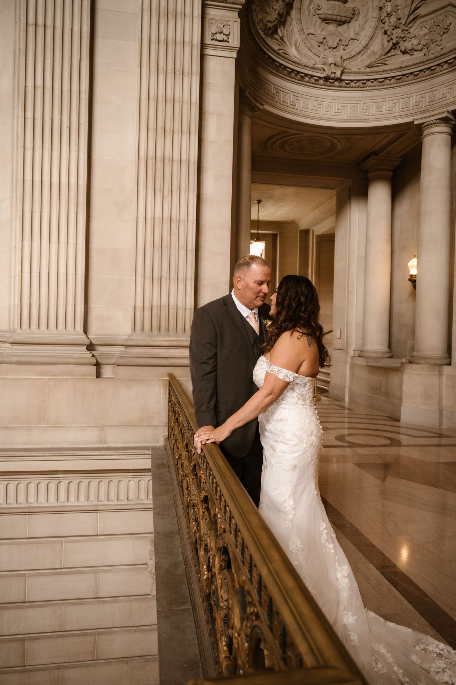 Wedding couple poses on ornate marble staircase in grand historic building with classical architecture.