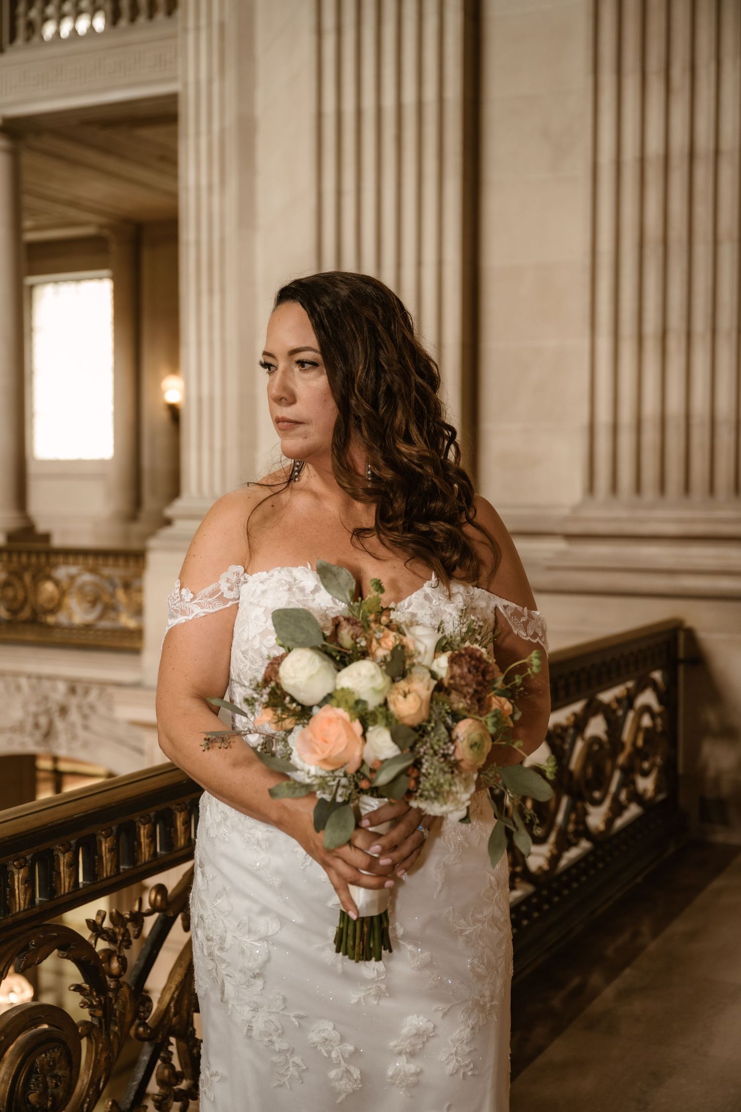 Wedding bouquet with peach and white flowers held against lace white dress.
