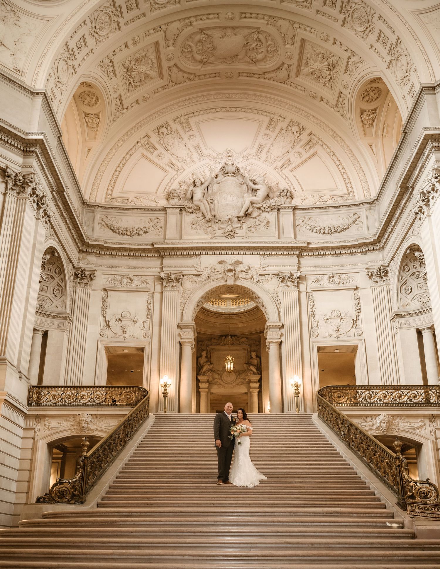 Panoramic view of ornate marble staircase with classical columns and decorated ceiling in historic building.