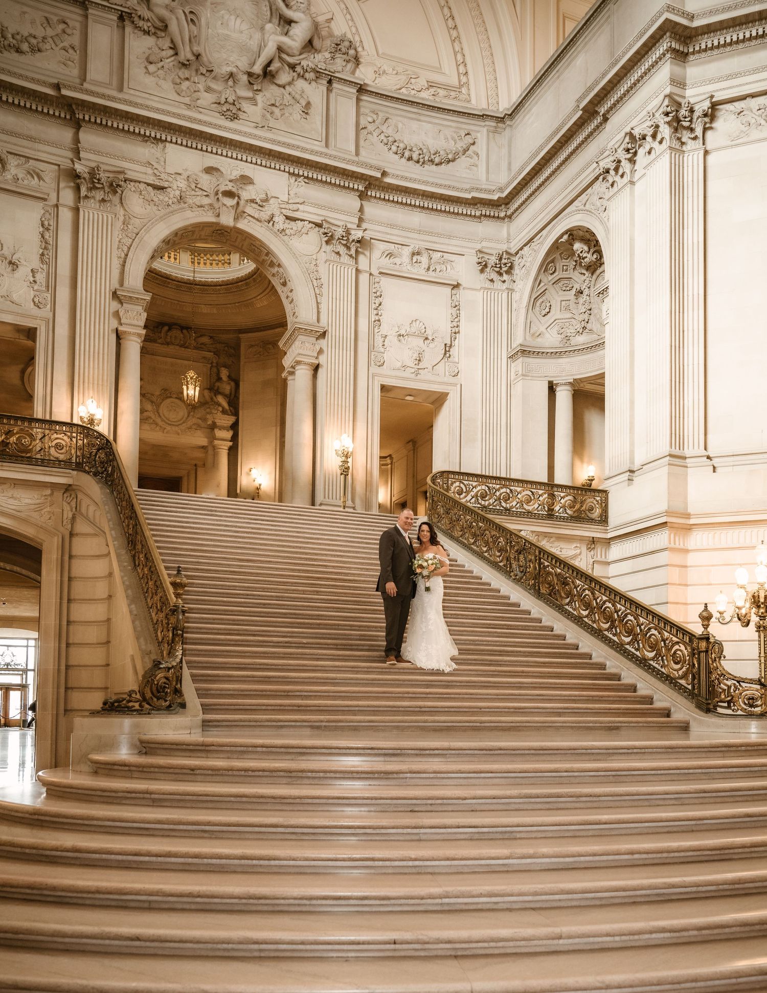 Wide angle shot of grand marble staircase with ornate architectural details and chandeliers.