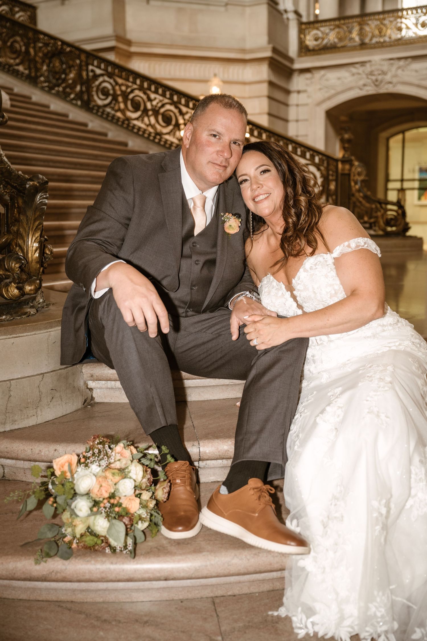 Wedding couple shares playful moment sitting on marble steps in historic building.