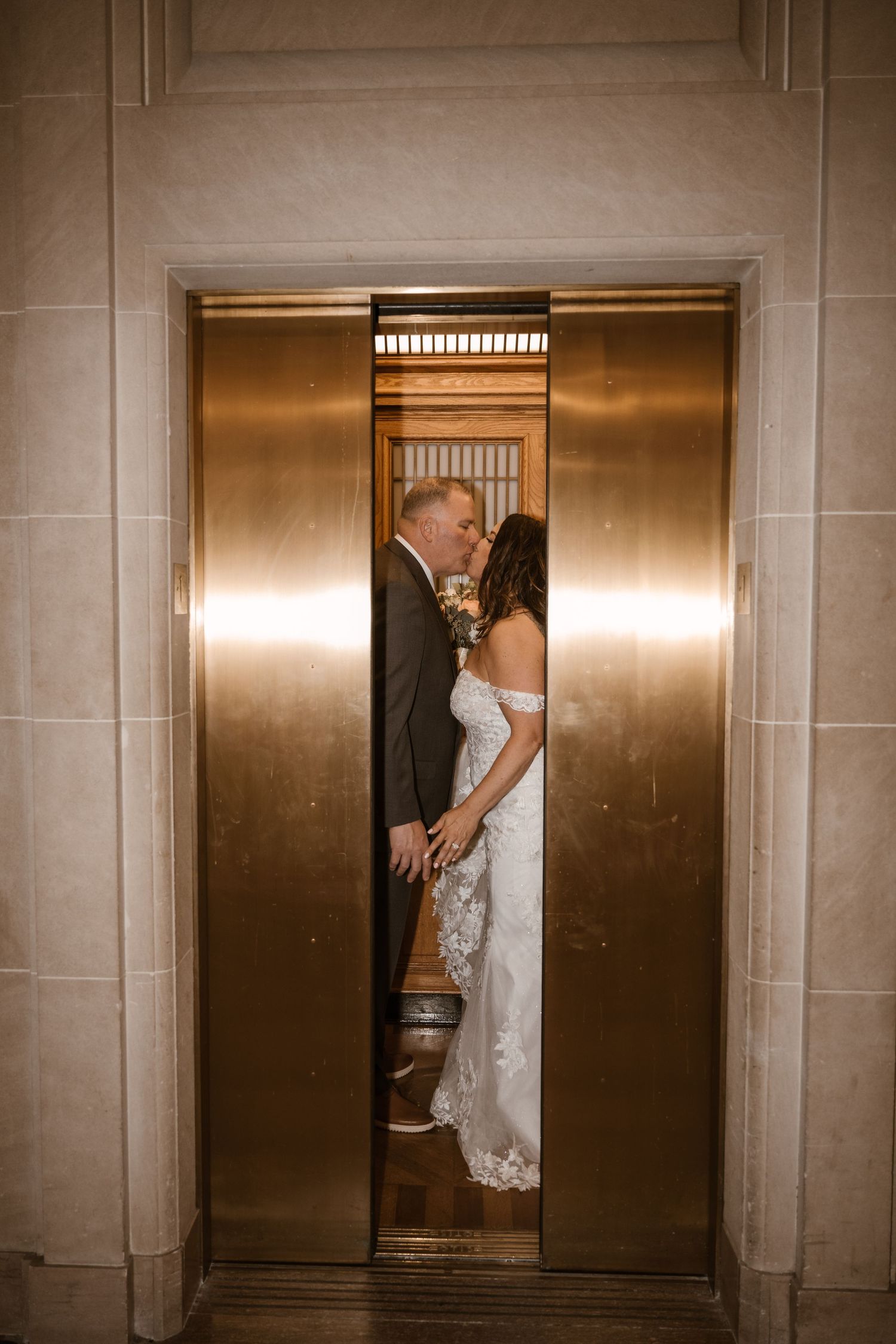Wedding couple shares intimate moment in golden elevator doorway.