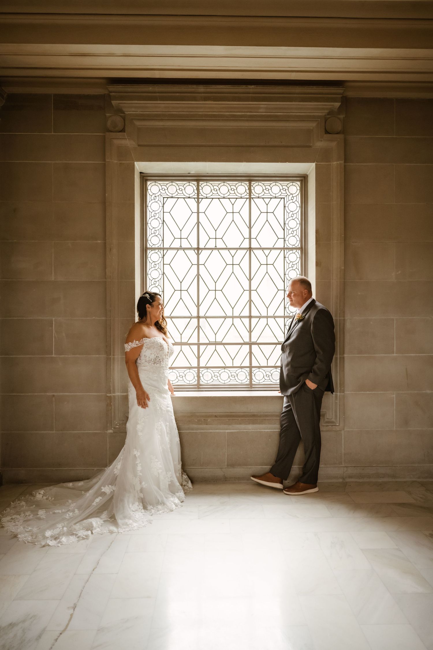 A romantic first look moment between a bride and groom in a sunlit room with a geometric window.