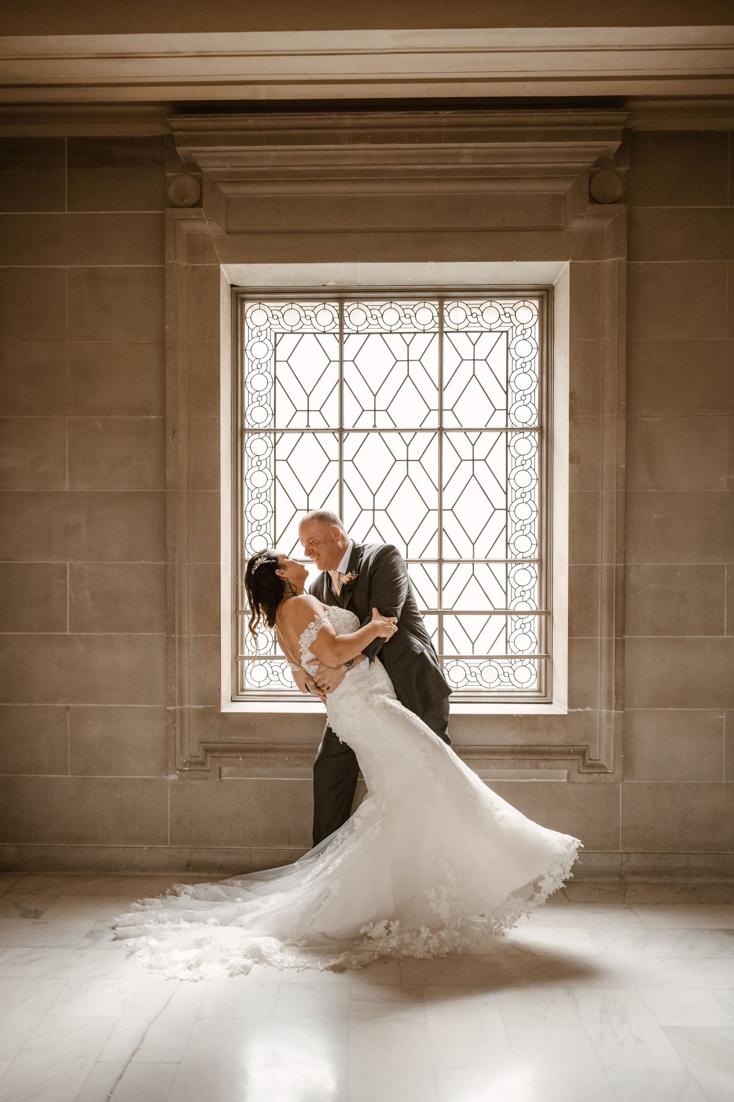 Wedding couple shares a romantic dance pose in front of a vintage window.