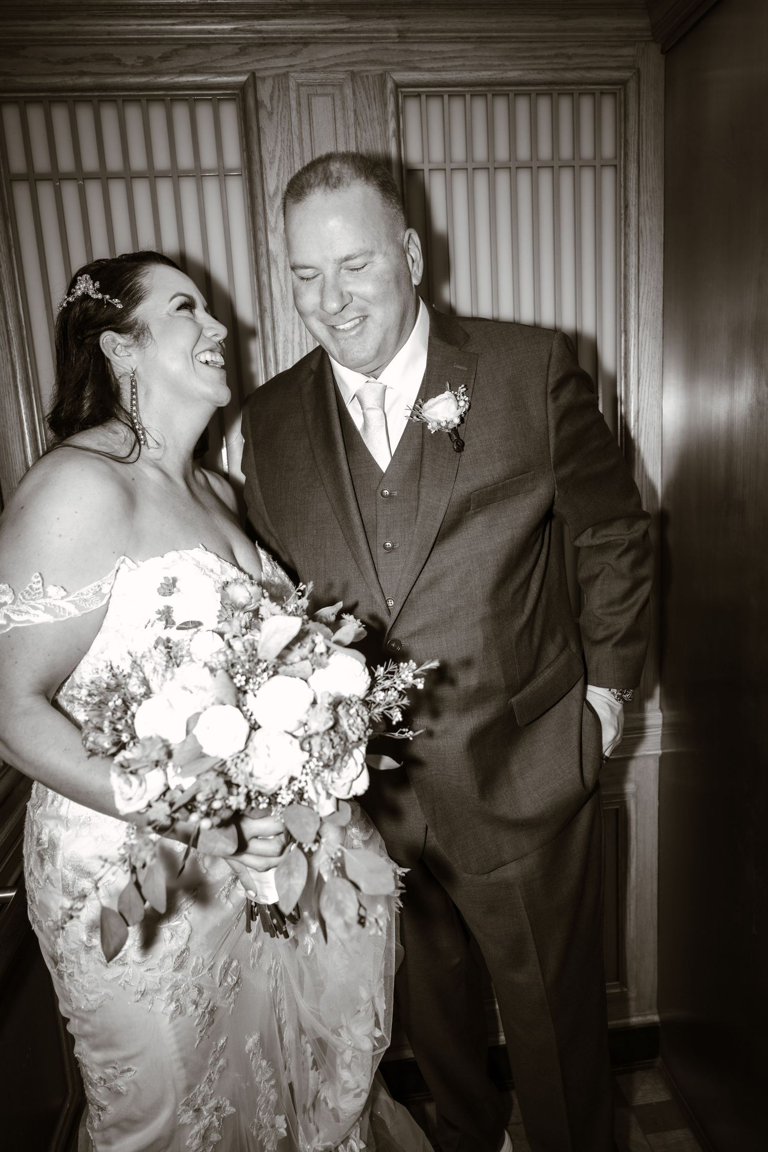 Black and white portrait of wedding couple sharing joyful moment with floral bouquet.