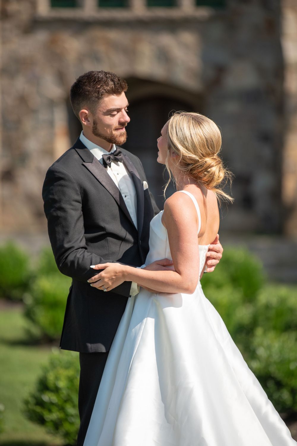 Newlyweds share a playful moment on the lawn of a historic stone building.