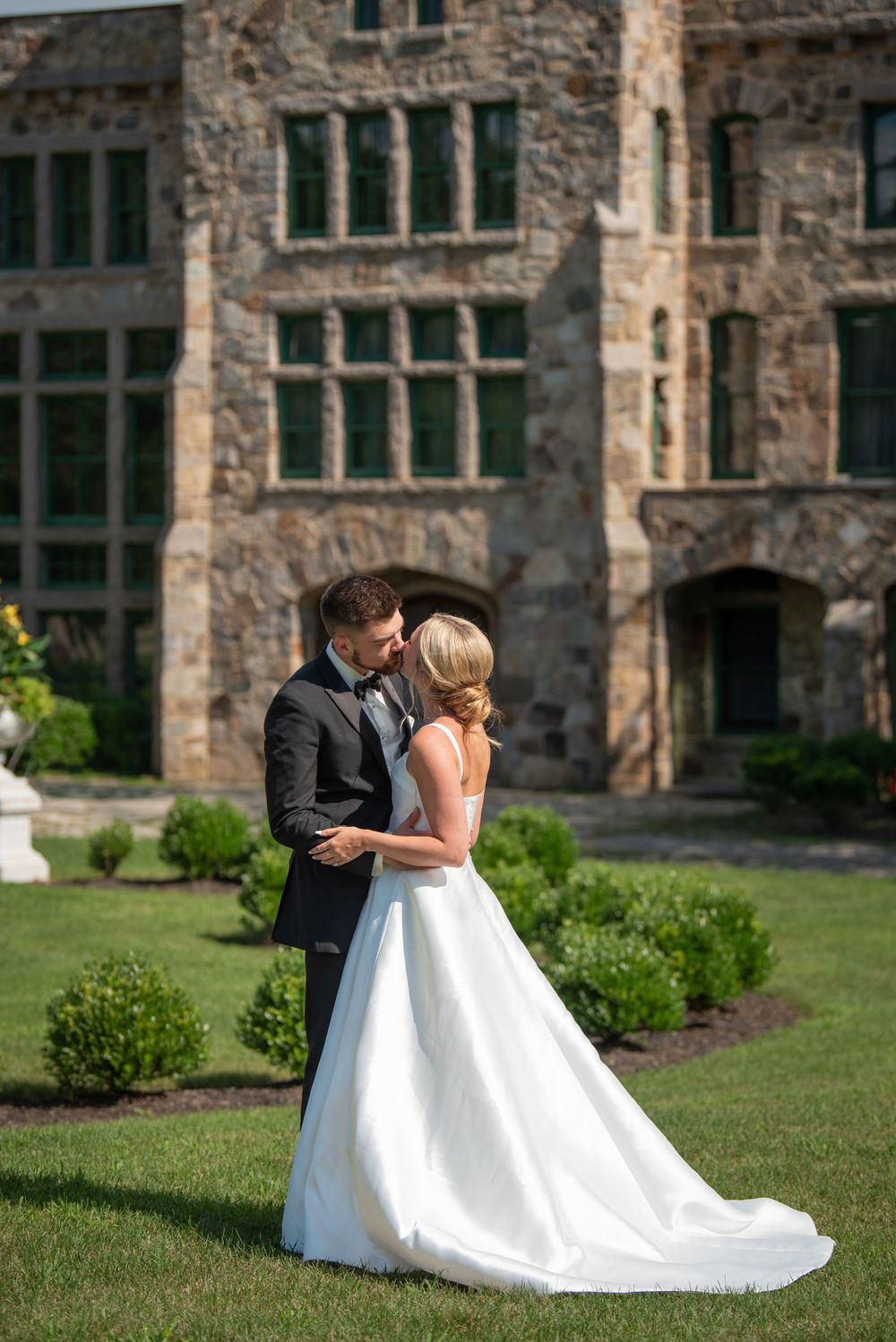 Bride in flowing white gown dances with groom on castle grounds.