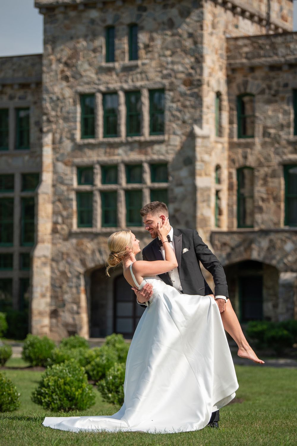 Playful wedding couple performs dramatic dip pose on castle grounds.
