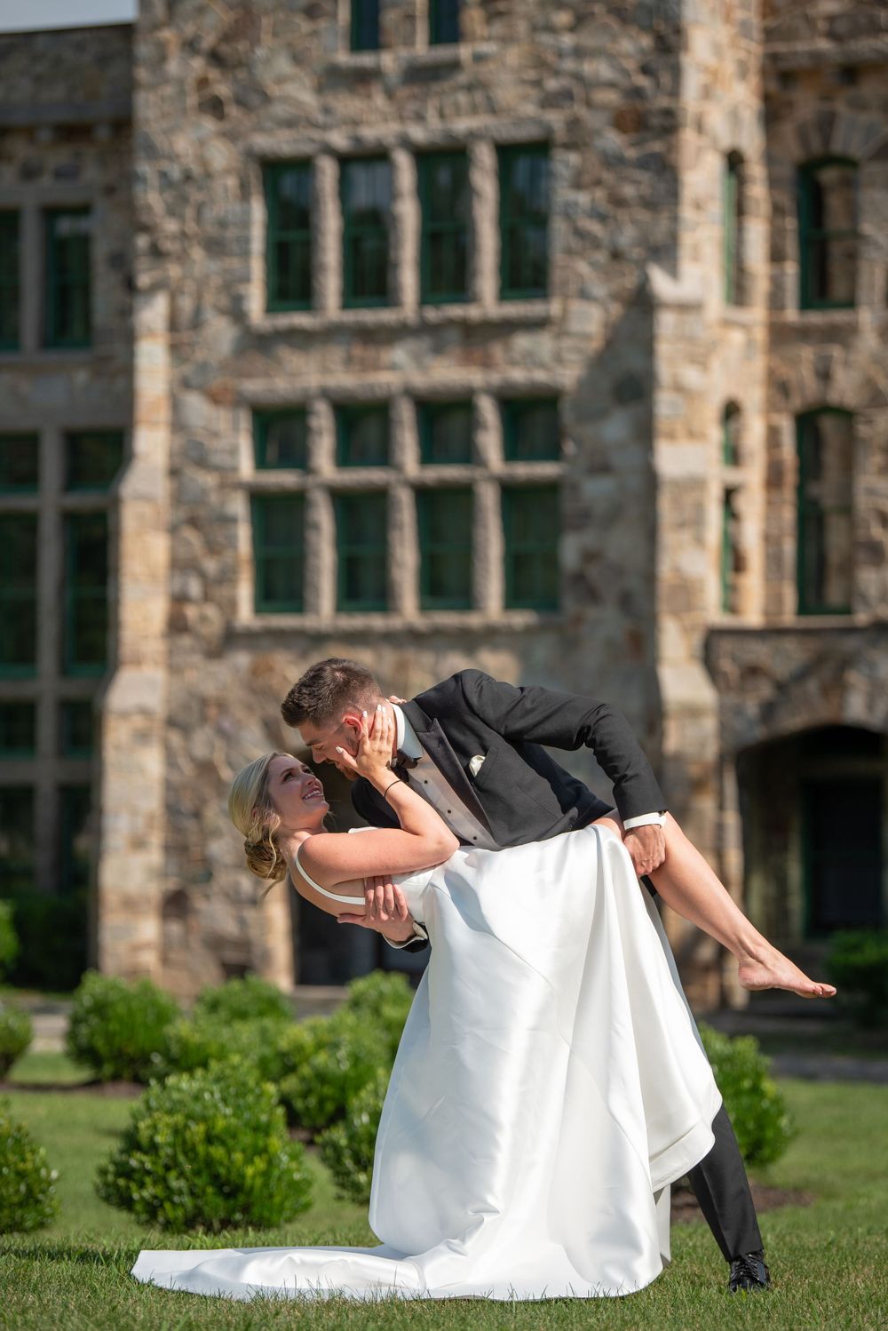 Newlyweds execute romantic dance dip pose on lawn by stone mansion.