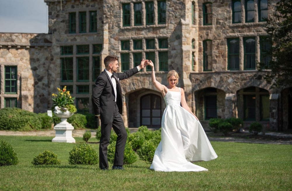 Panoramic view of wedding couple dancing on grounds of historic stone estate.