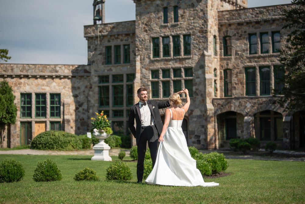 Bride and groom dance joyfully on lawn of elegant stone manor.