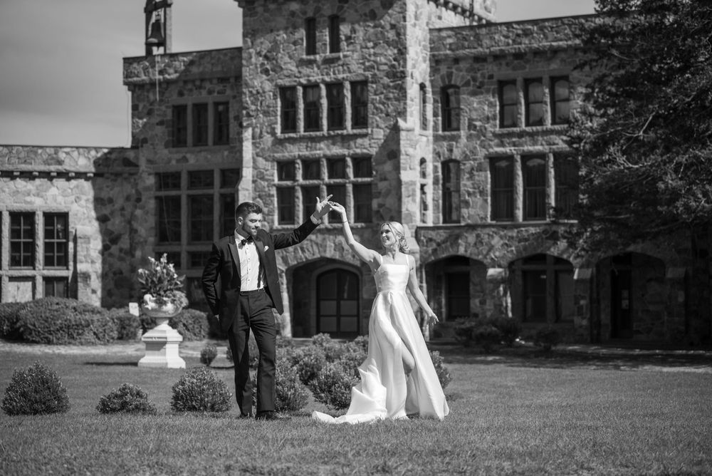 Black and white panorama of wedding couple dancing by stone architecture.