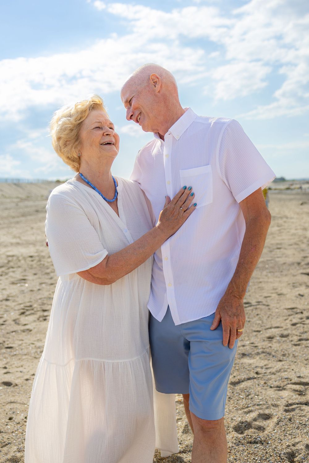 Happy senior couple sharing a romantic moment on a sandy beach, dressed in white summer clothing on a sunny day.