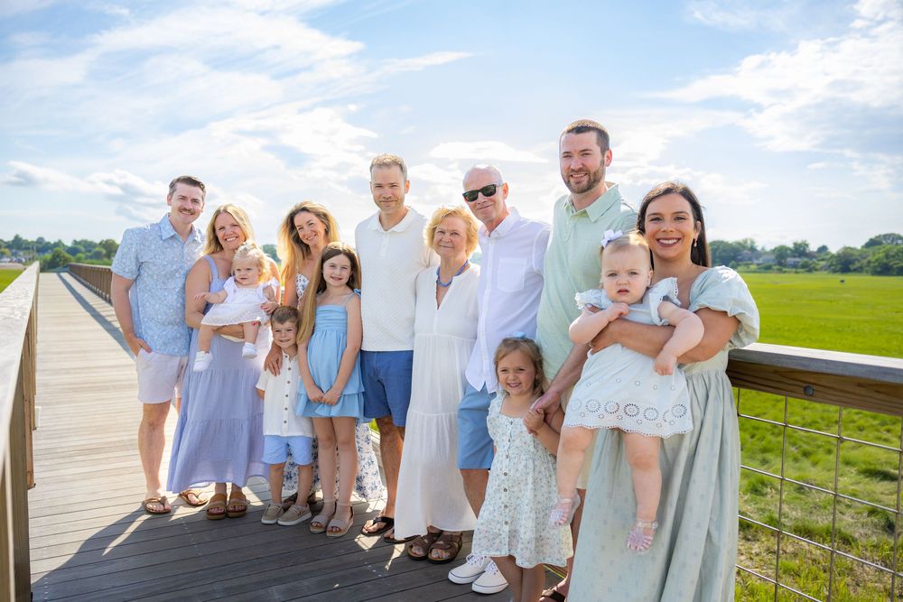 Large family group portrait on a wooden boardwalk overlooking a green marsh on a sunny day.
