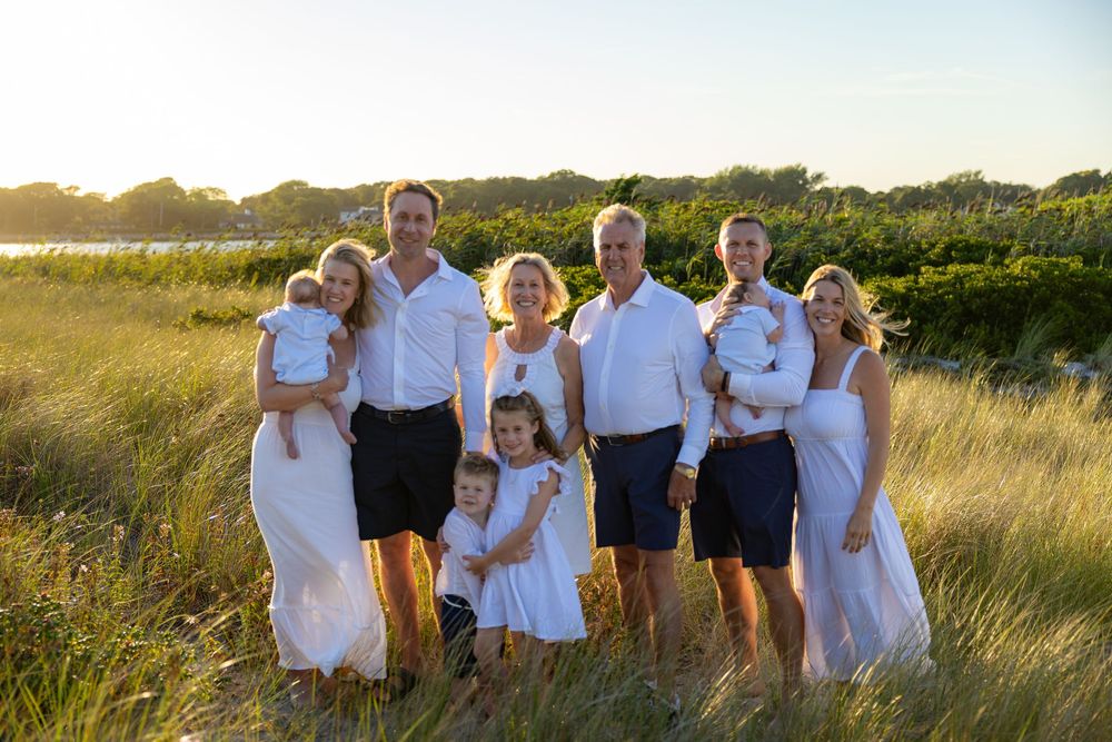 Group wearing white and navy outfits poses together in a golden field at sunset.
