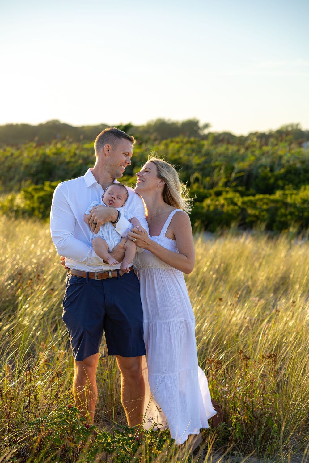 A couple shares tender moments in a golden field at sunset while wearing white and navy blue outfits.