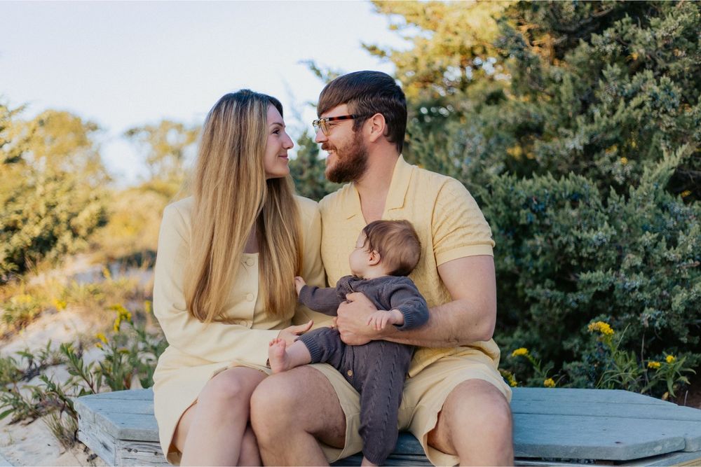 A couple sits together on a blue bench in a park during golden hour with autumn foliage in the background.