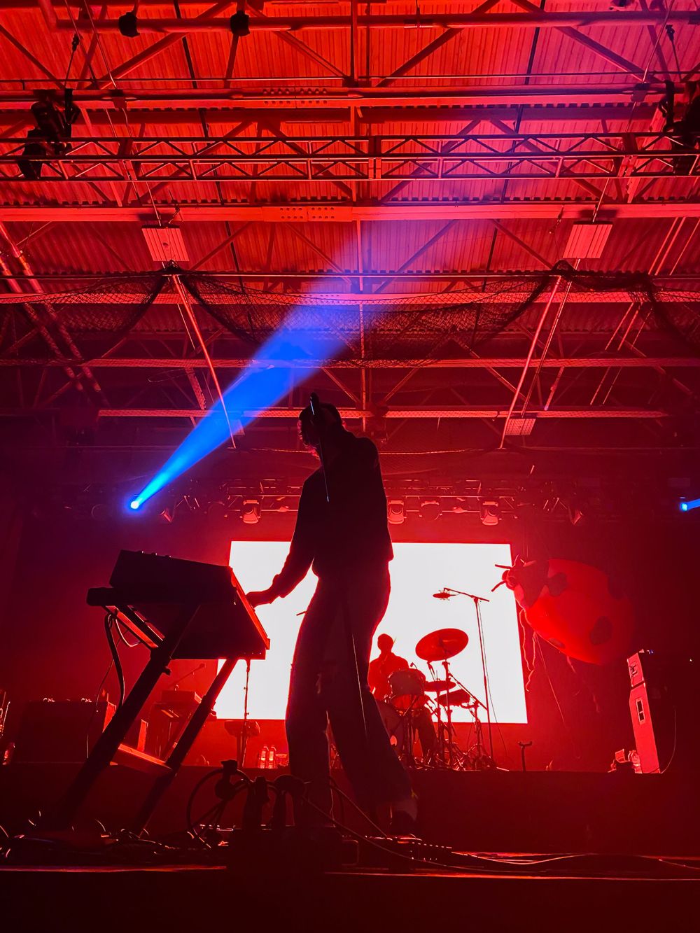 Silhouetted performer on stage backlit by dramatic red lighting and blue spotlights during a concert performance.