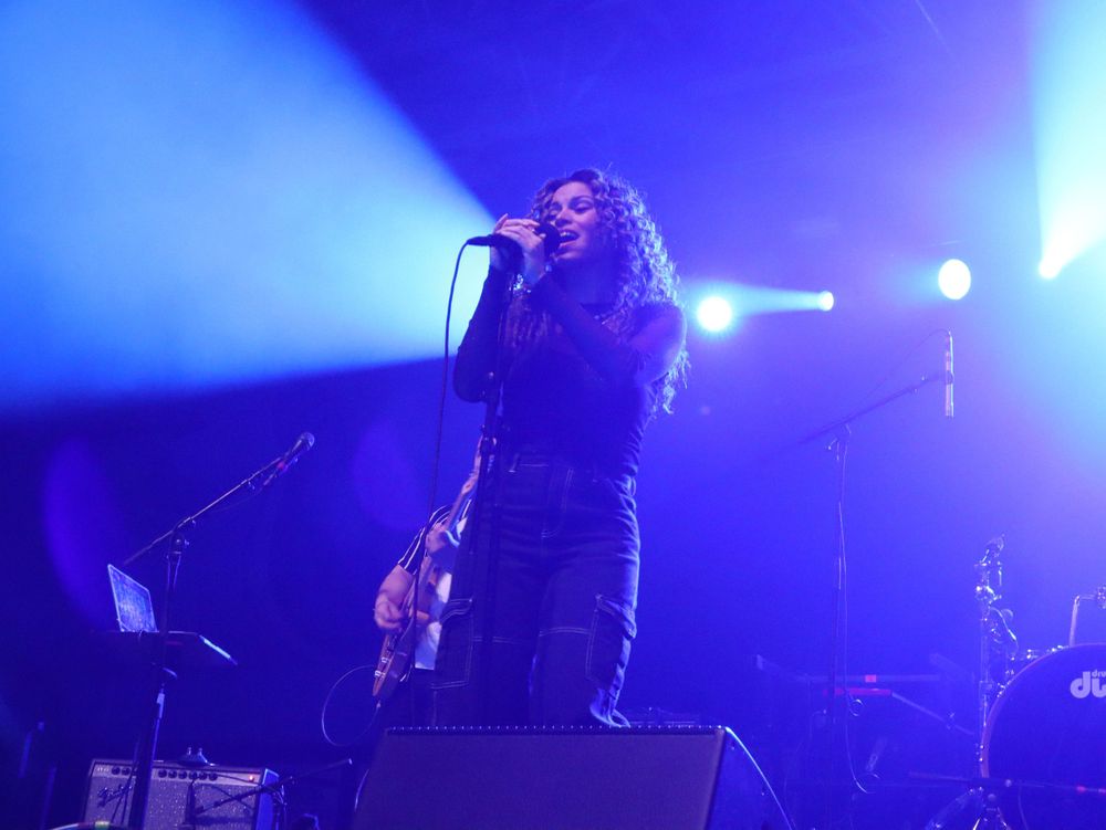 Concert performer silhouetted in blue stage lighting singing into microphone during live music performance.