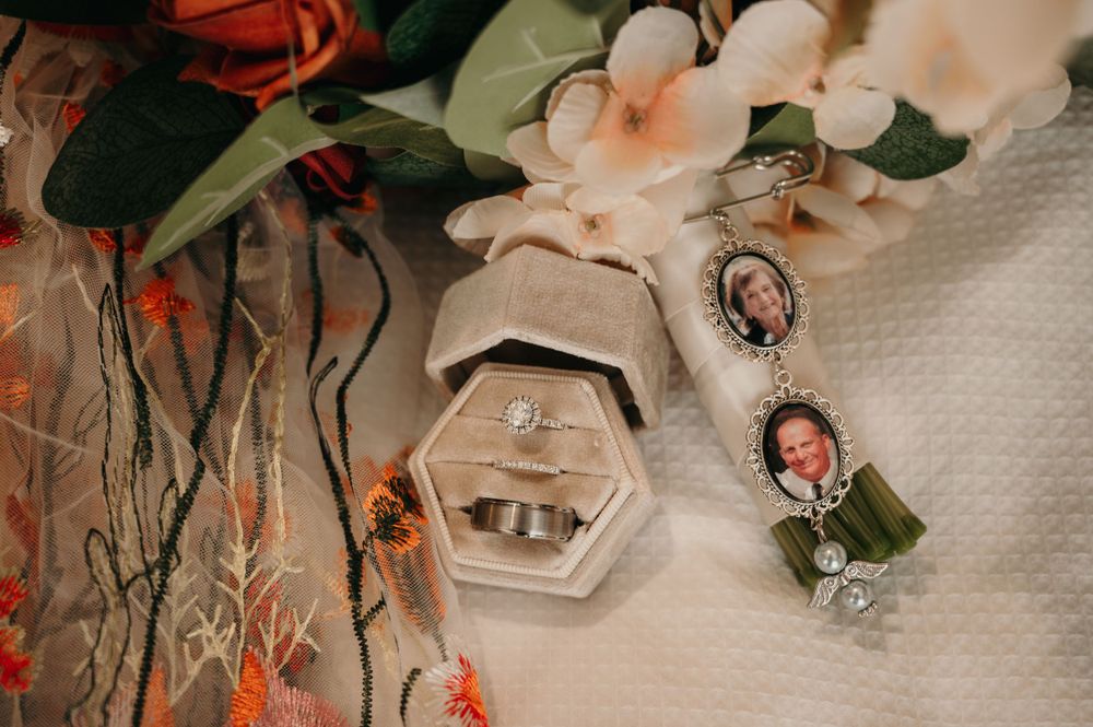Wedding rings and photo charm bouquet accessories displayed in a hexagonal velvet ring box.