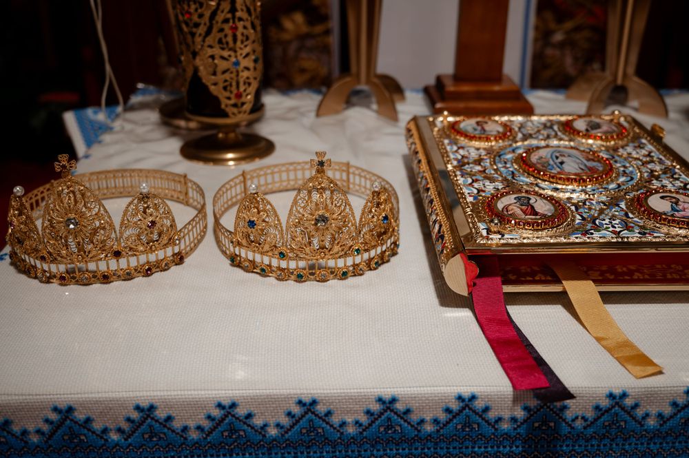 Golden wedding crowns and ornate Bible displayed on white embroidered cloth for Orthodox ceremony.